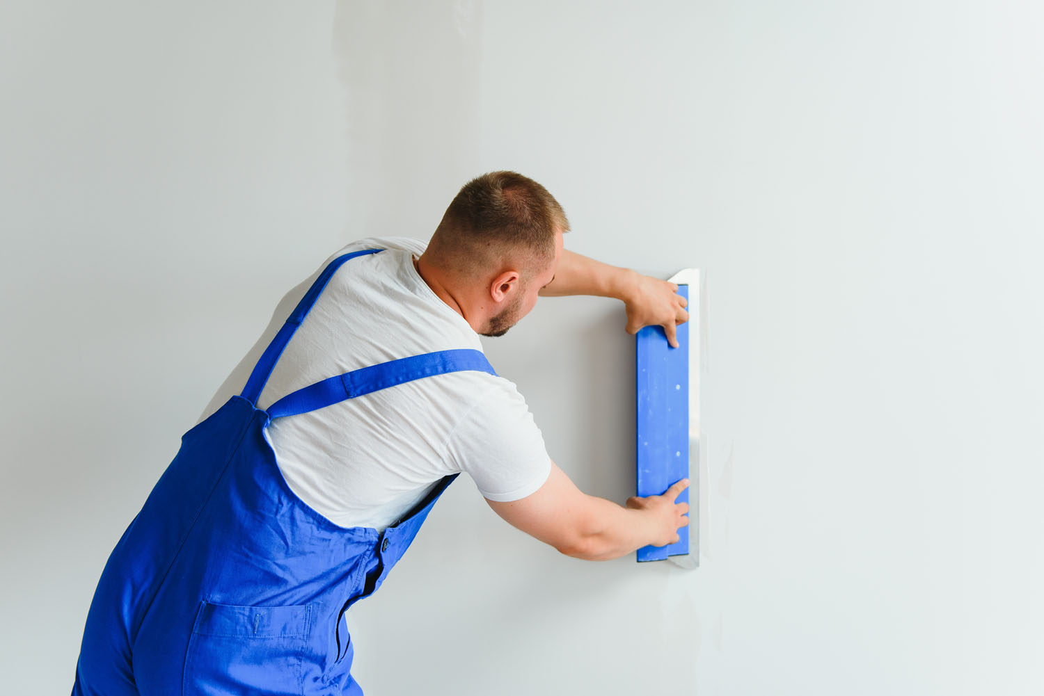 Plasterer smoothes the wall surface with a wall grinder. Master builder grind a white plaster wall. a man in overalls grinds the surface in a respirator. experienced repairman
